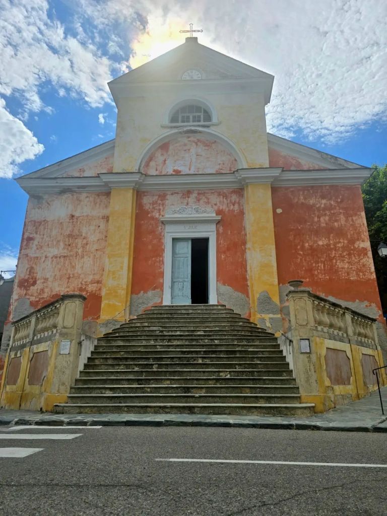 Église Sainte-Julie de Nonza, surplombant la mer en Haute-Corse, avec son clocher élancé et ses façades colorées.